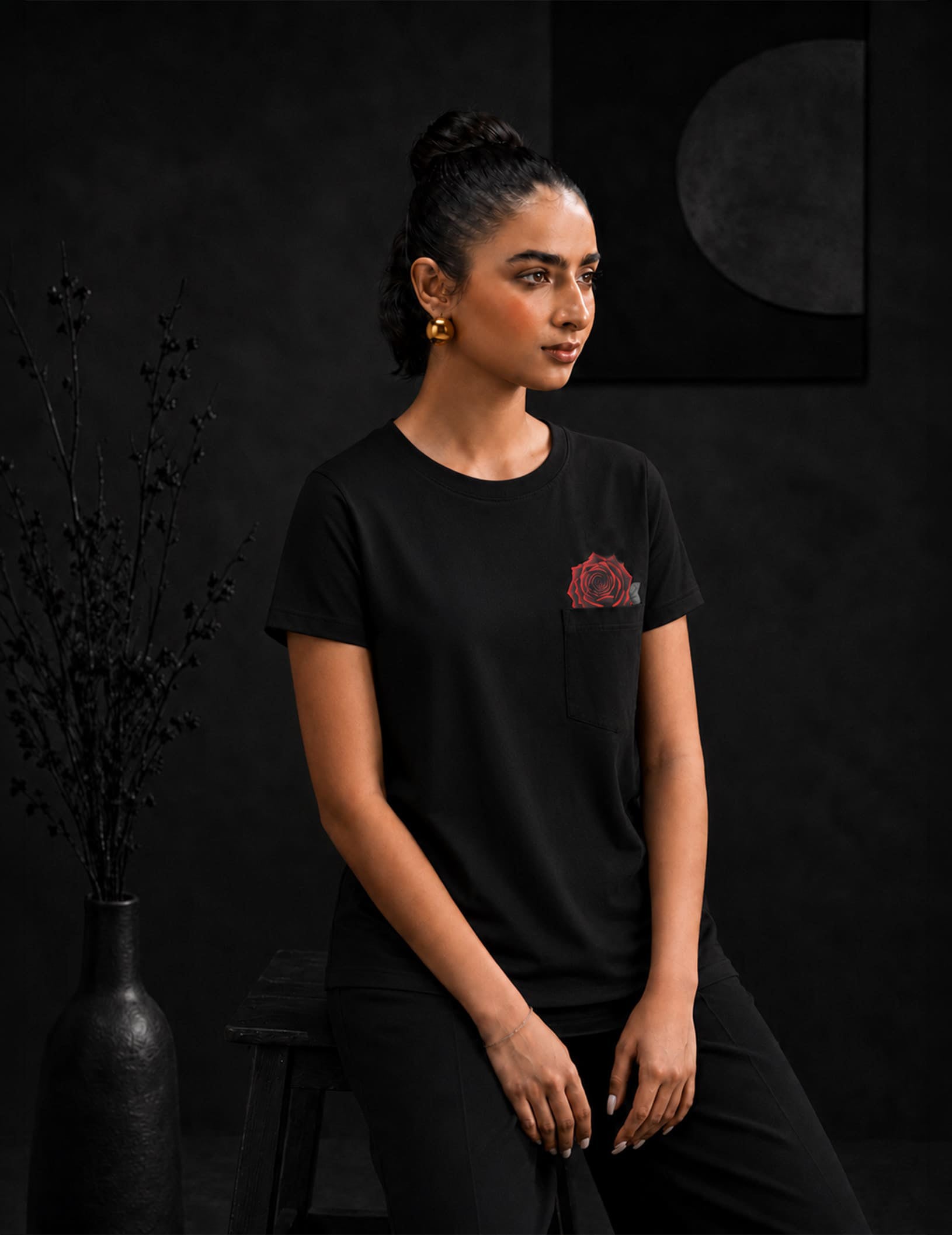 Female model wearing the BLACOIR Rosemark Pocket Tee with signature red rose pocket detail, captured in a luxury editorial setting with modern minimalist styling.
