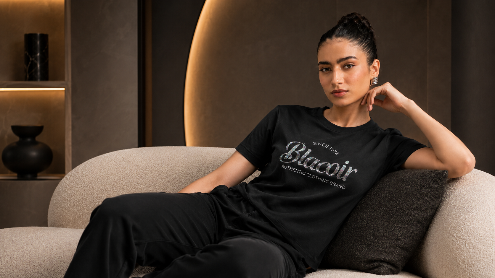 Blacoir women’s black glitter logo t-shirt from The Core Edit styled on a modern sofa in a premium lifestyle fashion banner